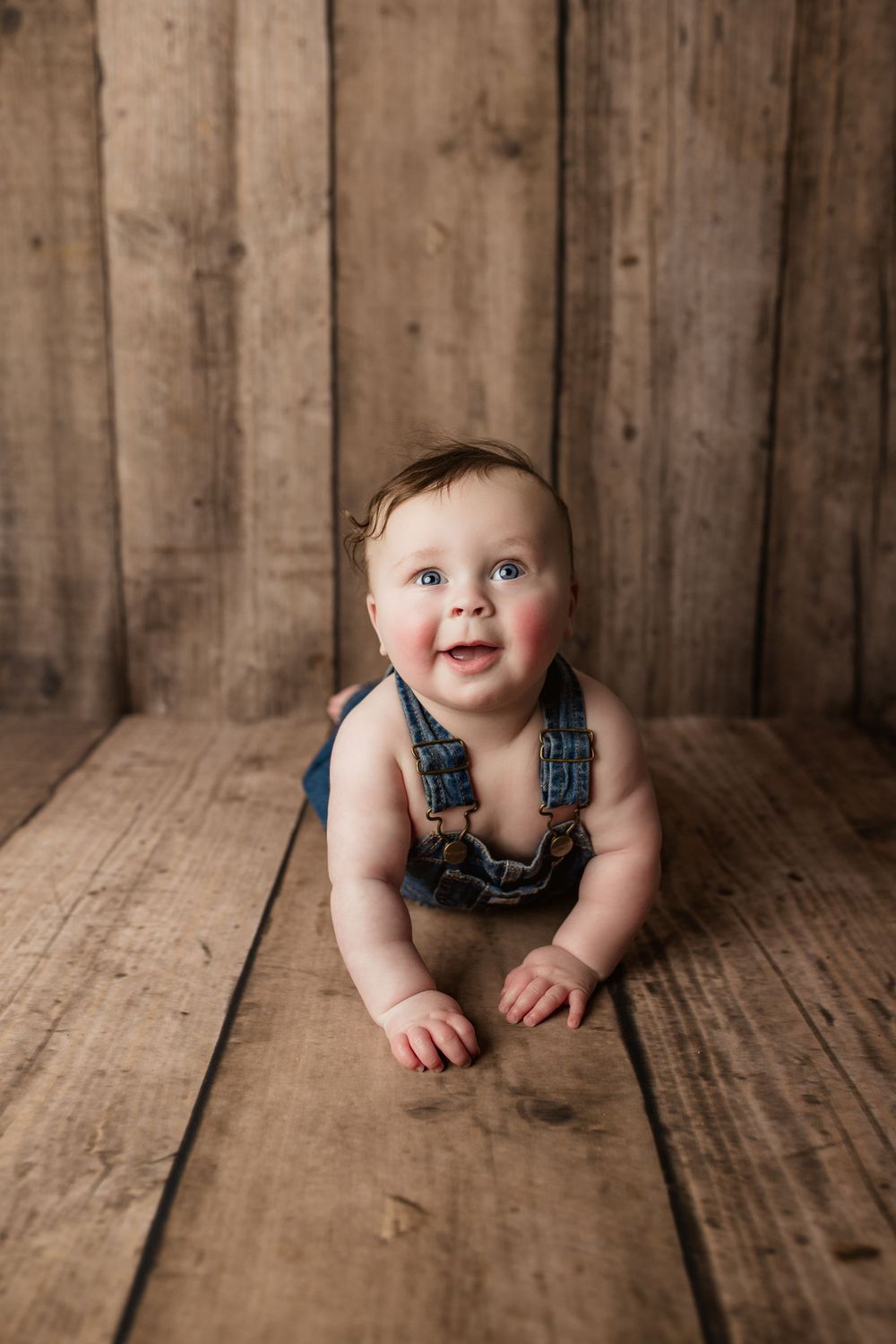 Rustic wooden backdrop photo shoot featuring denim overalls and joyful expression.