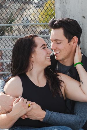 A couple smile at each other. The man has his arms wrapped around the woman and her hand is on his neck.