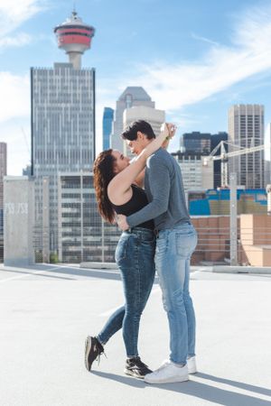A couple on a parkade hug. The woman has her arms around his neck. Calgary tower in the background.