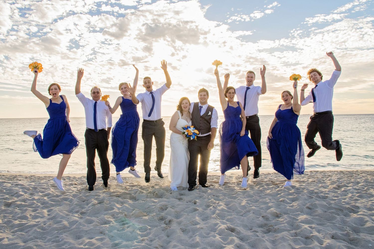 fun photo of bridal party jumping in the air at the beach