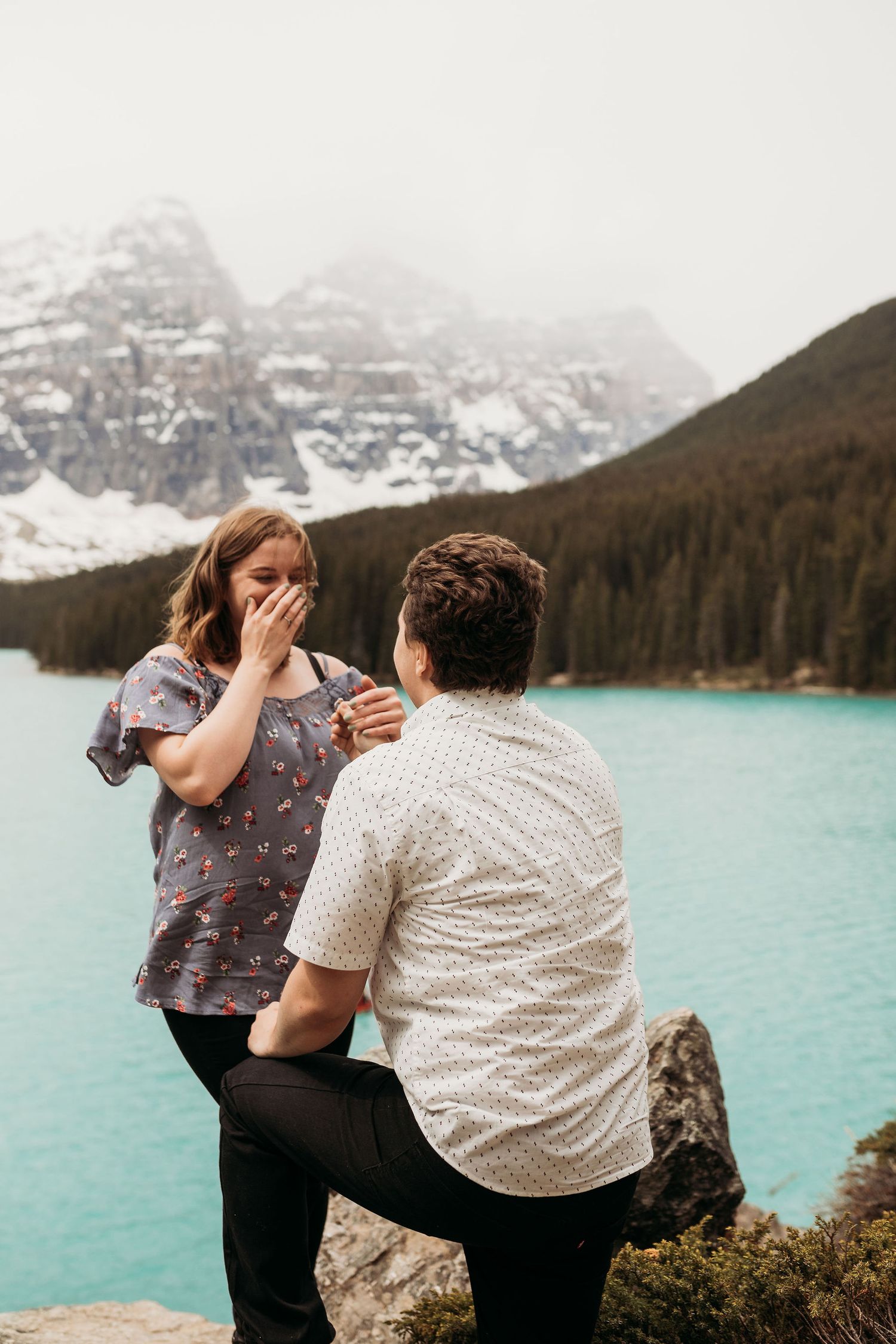A surprise proposal moment captured at Moraine Lake in Banff National Park with snow-capped mountains in the background.