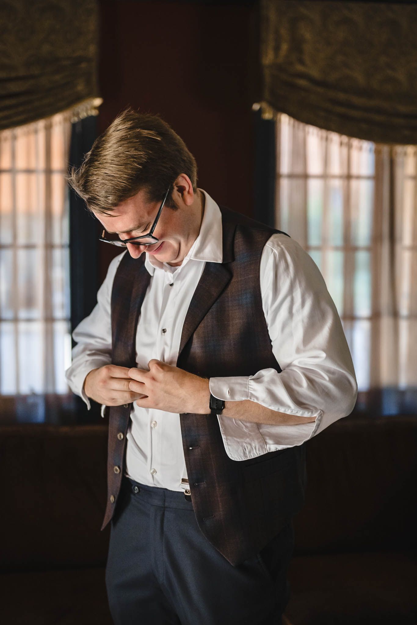 A person in formal attire adjusts their tie while getting ready in a dimly lit room.