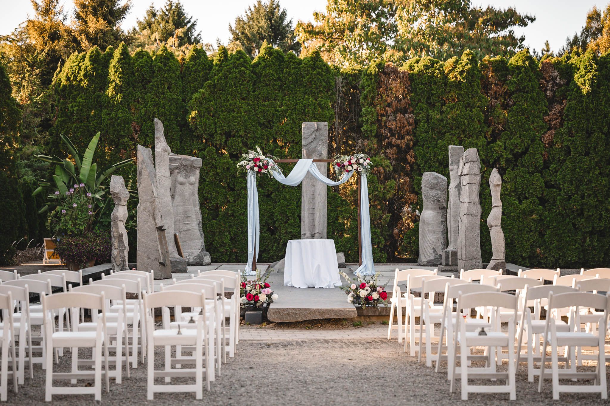 White wooden chairs arranged in rows for an outdoor garden wedding ceremony.
