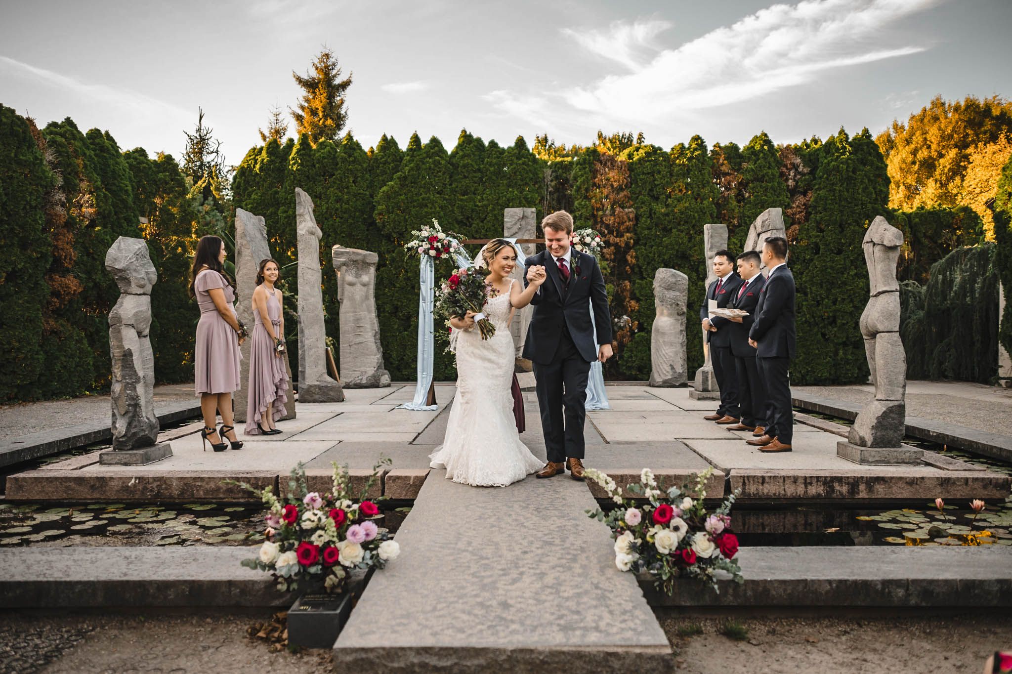 Panoramic view of outdoor wedding ceremony with stone columns and forest backdrop.