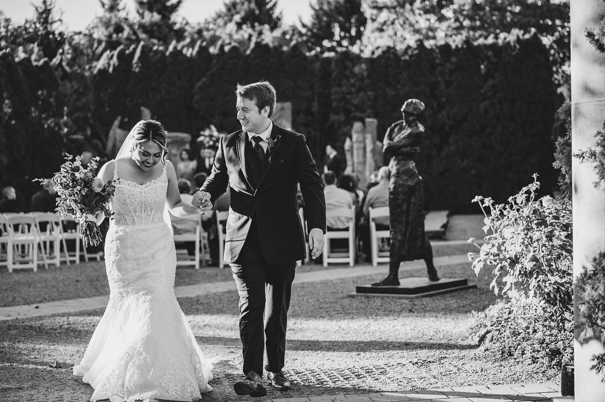 Wedding ceremony in progress with guests seated in white chairs on stone patio.