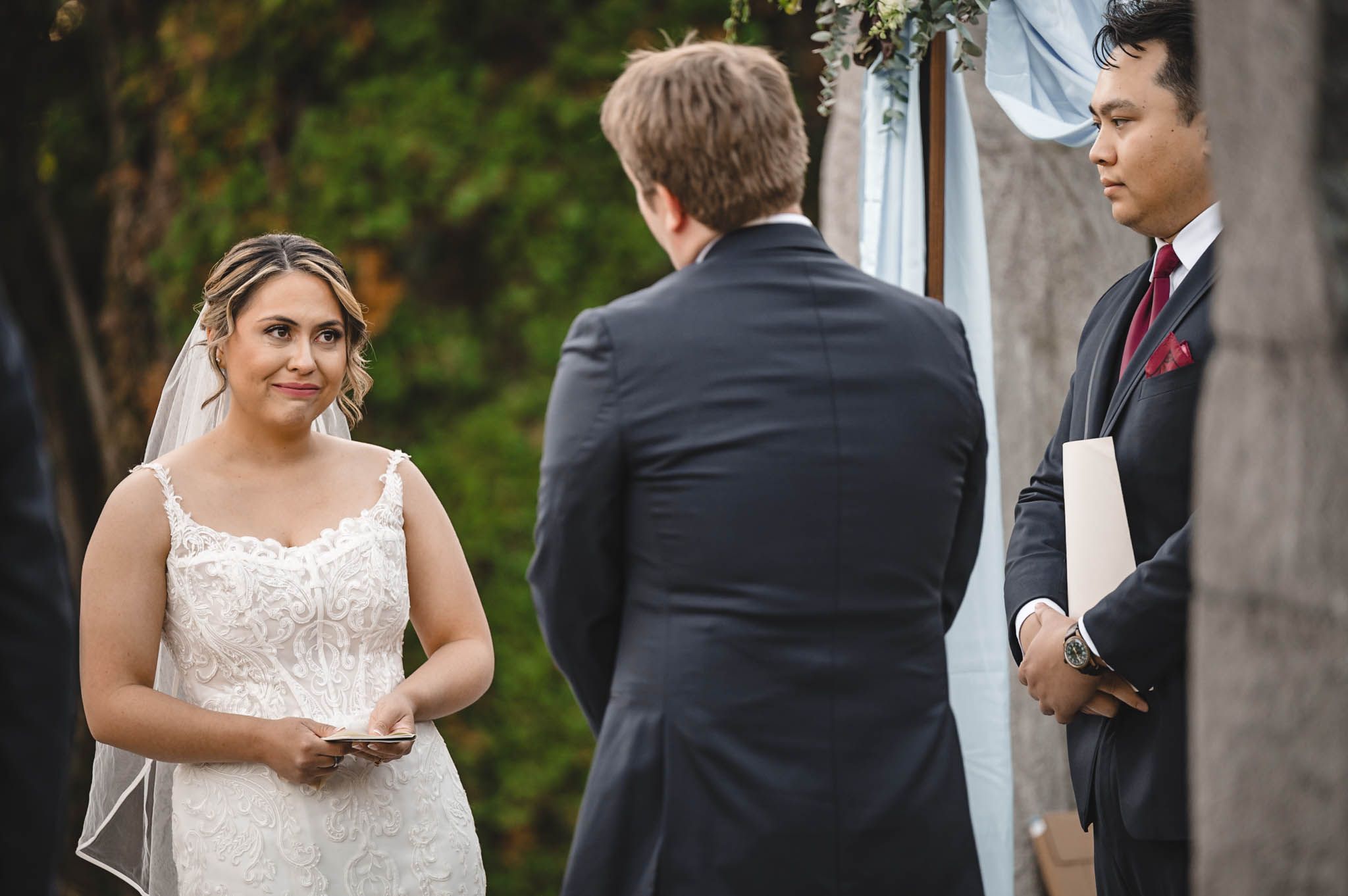 Elegant outdoor wedding ceremony with light blue and burgundy accents against natural greenery.