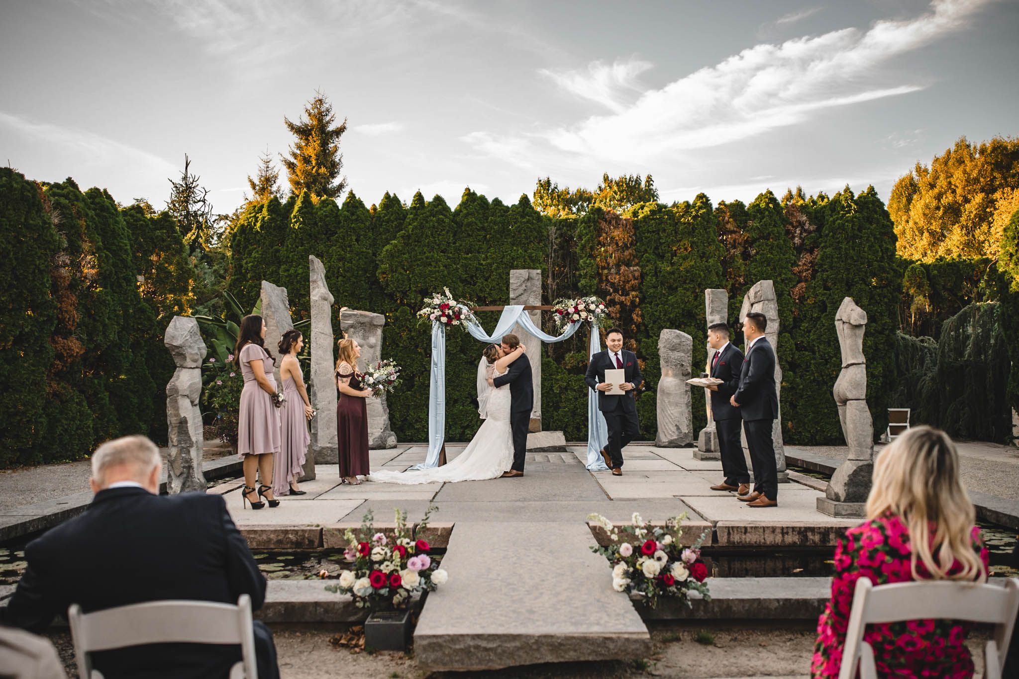 Sunset wedding ceremony with white chairs and stone columns creating a romantic outdoor aisle.