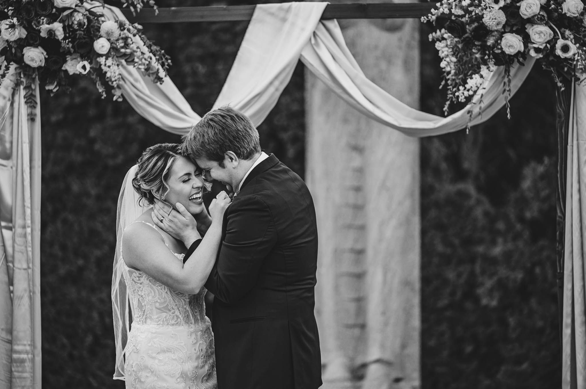 Black and white wedding ceremony photo with elegant white draping and floral decor.