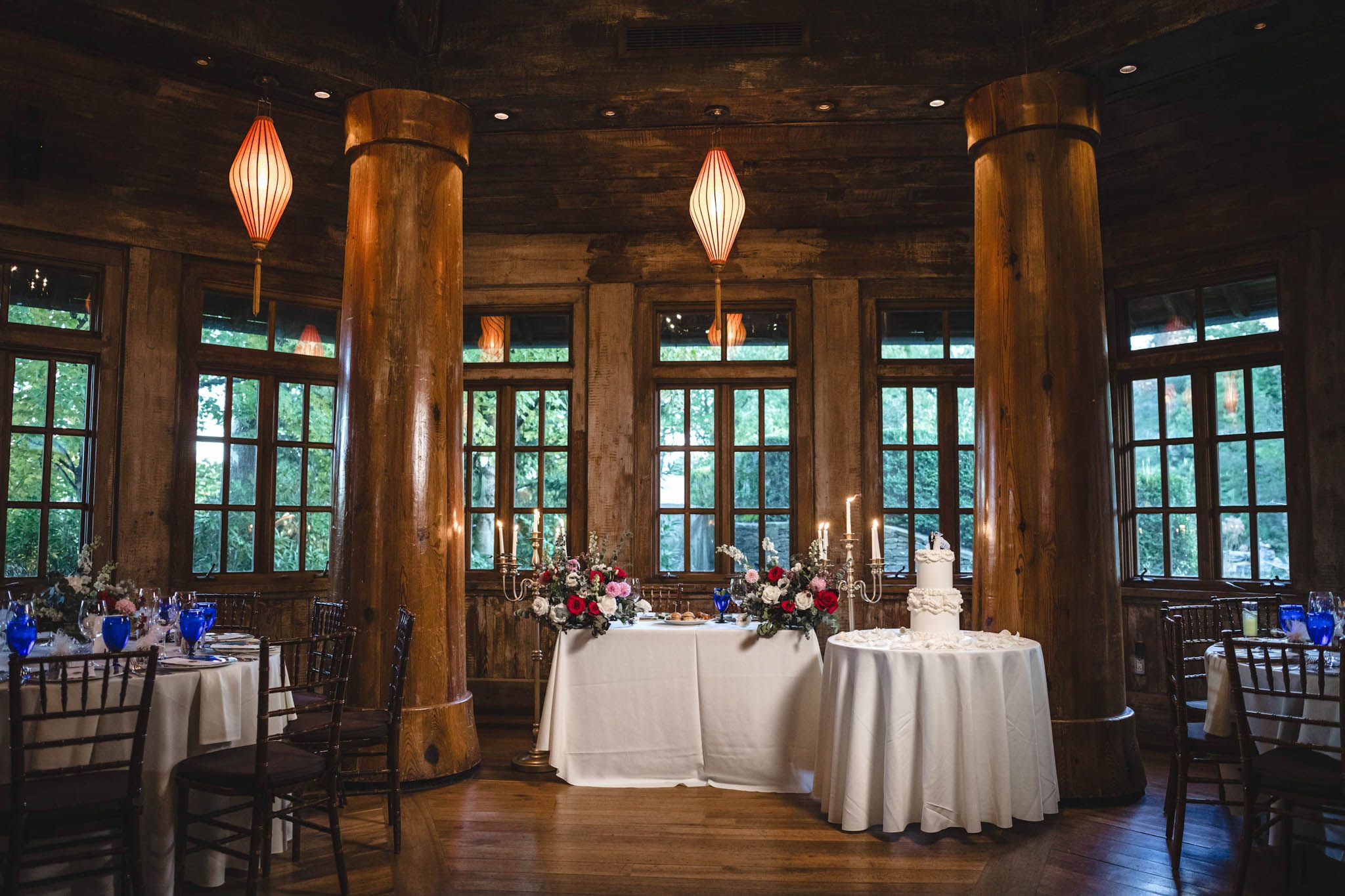 Rustic wooden reception hall with elegant lighting and white tablecloths.