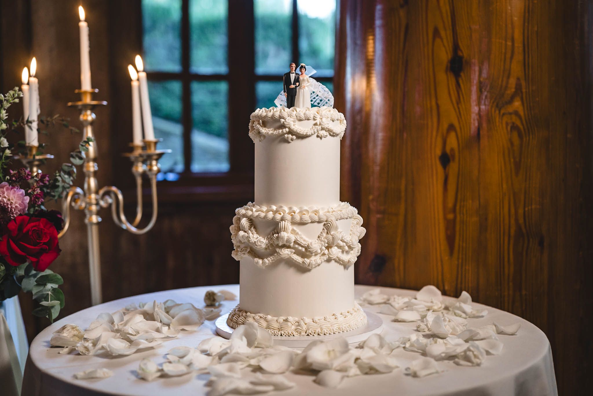 Elegant wedding cake display with candelabras in rustic wooden venue.