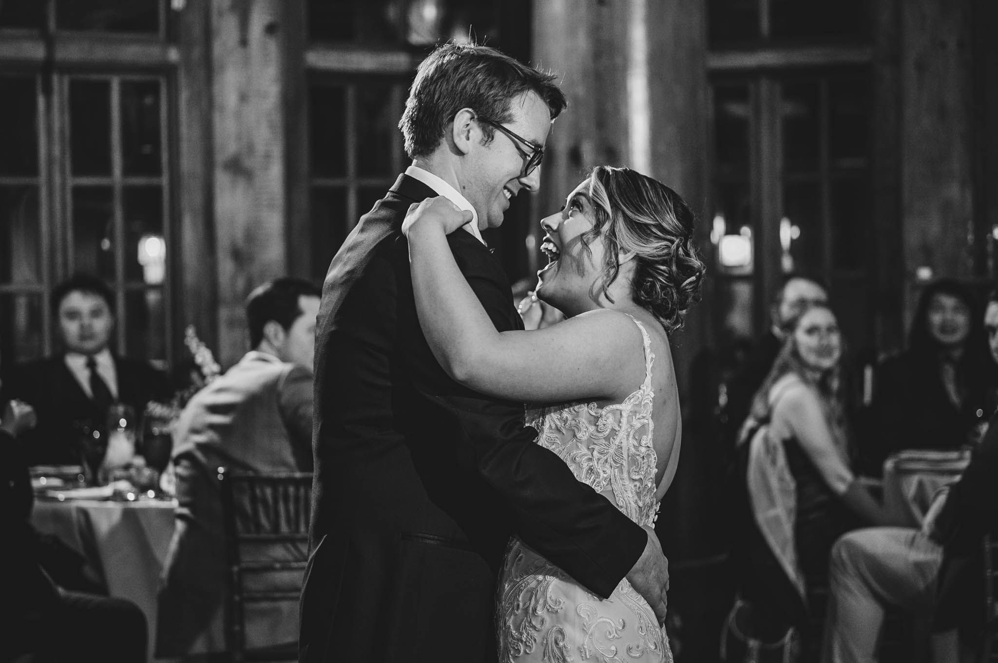 Black and white photo of couples dancing at an elegant wedding reception in a wooden hall.