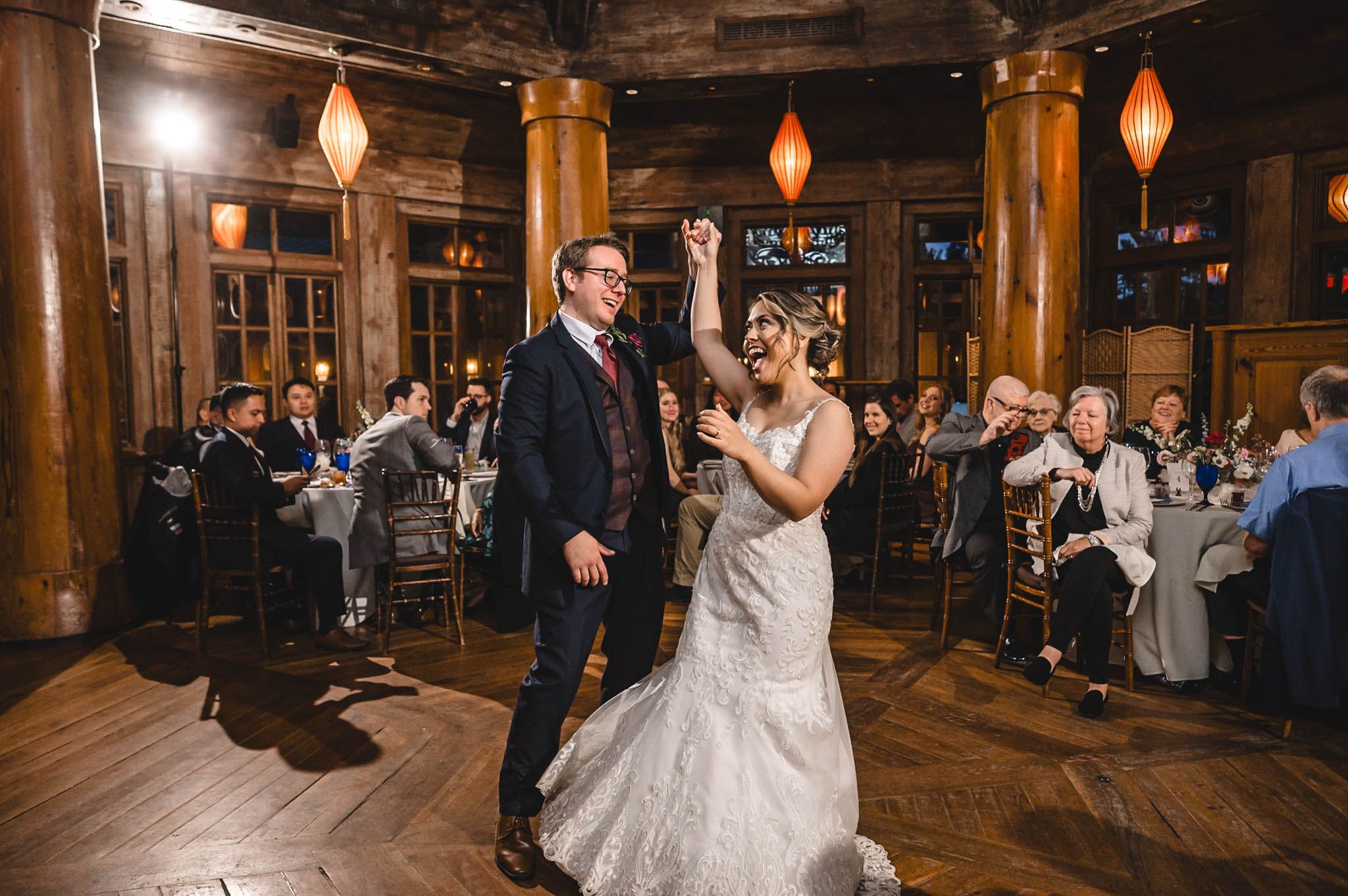 Wedding celebration in a timber-framed venue with orange lanterns and dancing guests.