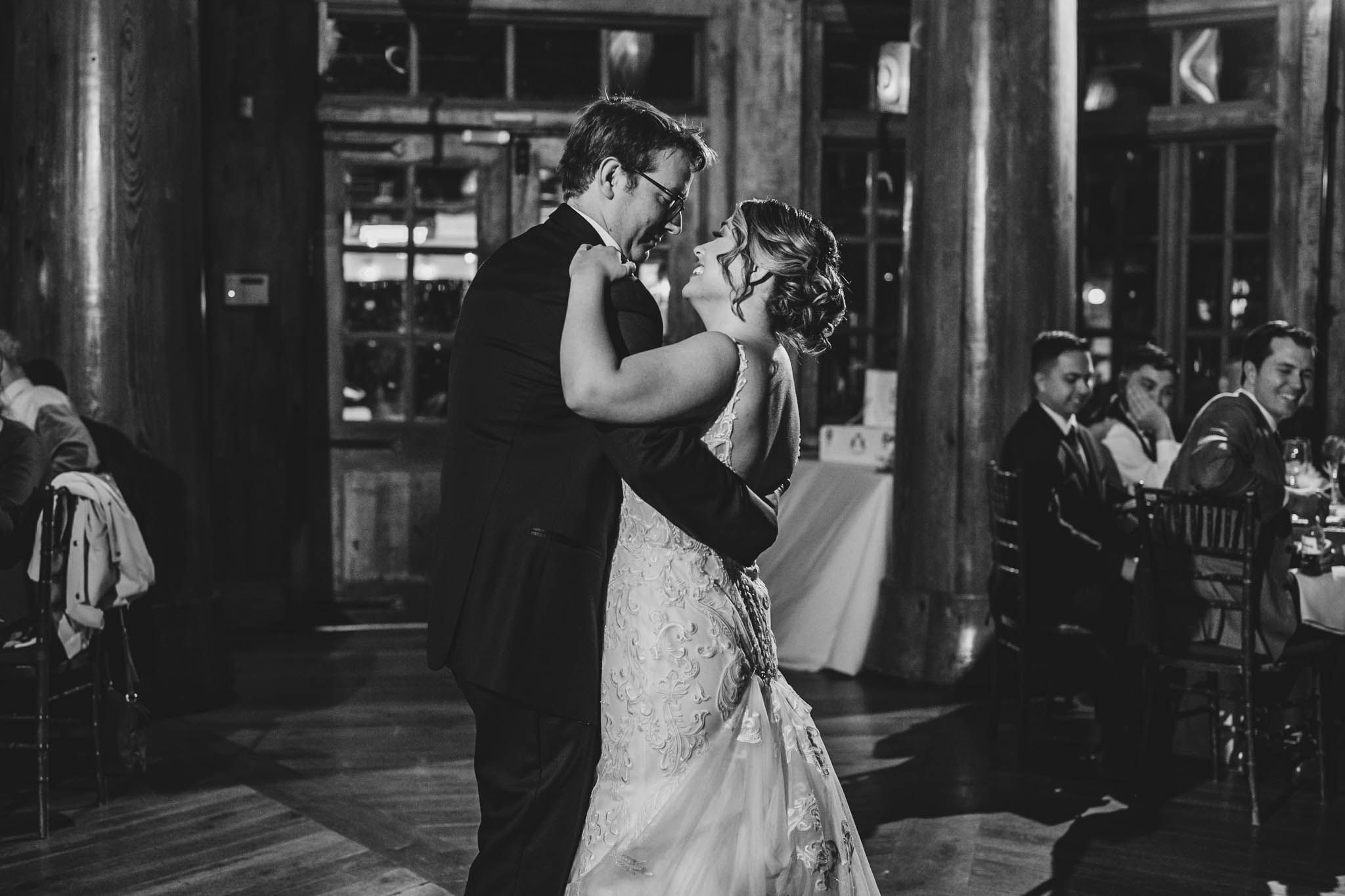Couples dancing at an evening wedding reception in a dark wooden interior with ambient lighting.