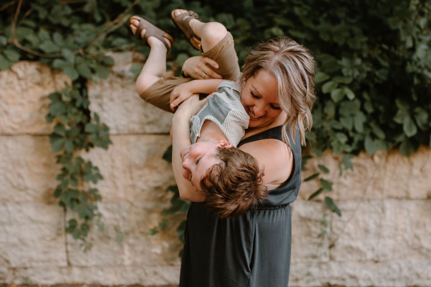 Playful outdoor portrait against stone wall with natural greenery.