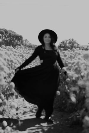 A black and white portrait of someone twirling in a long dress amidst flowering bushes.