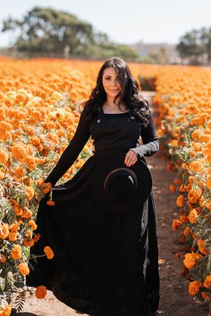 A person in a flowing black dress stands elegantly in a field of orange marigolds.