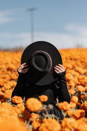 Creative portrait hiding behind a black hat in a field of orange marigolds.