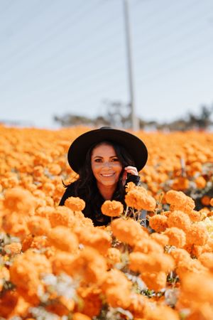 Joyful autumn portrait in a field of orange marigolds wearing a black hat.