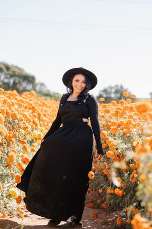 A person wearing a black dress stands gracefully in a field of bright orange marigolds.