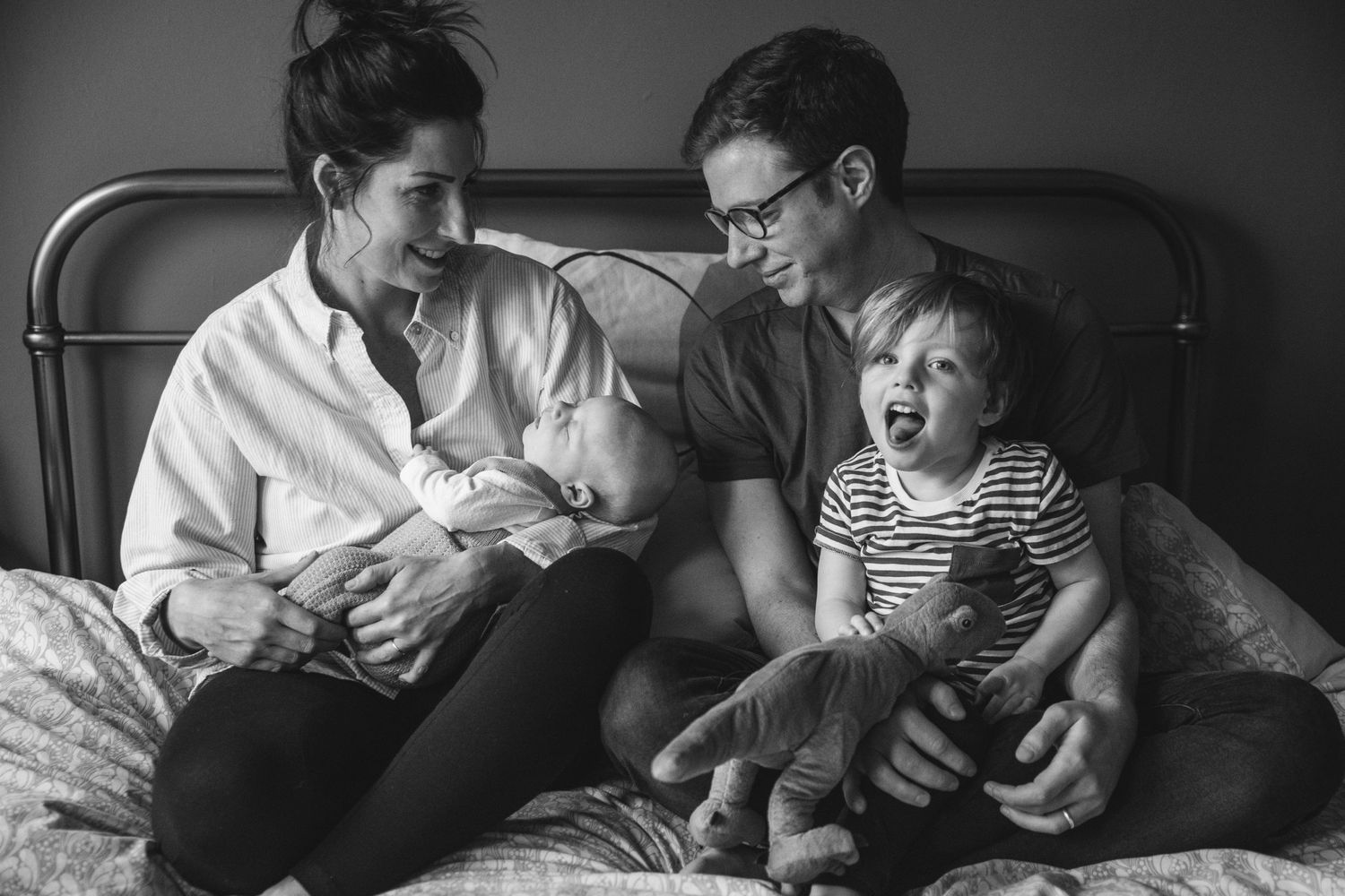 A family shares an intimate moment together on a bed while bonding with their baby and toddler in black and white.