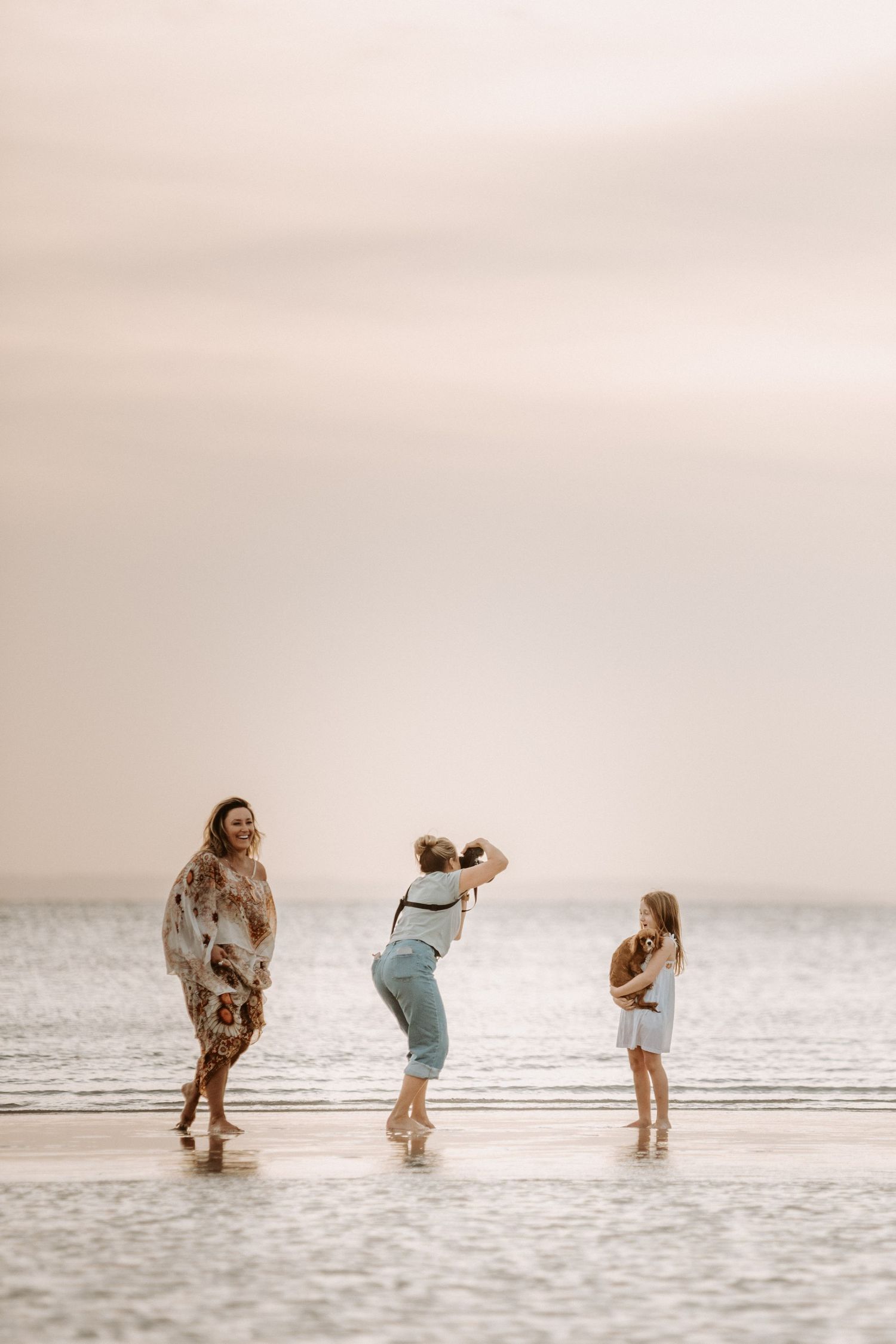 Joyful beachside scene with three people playing and jumping in shallow ocean water.