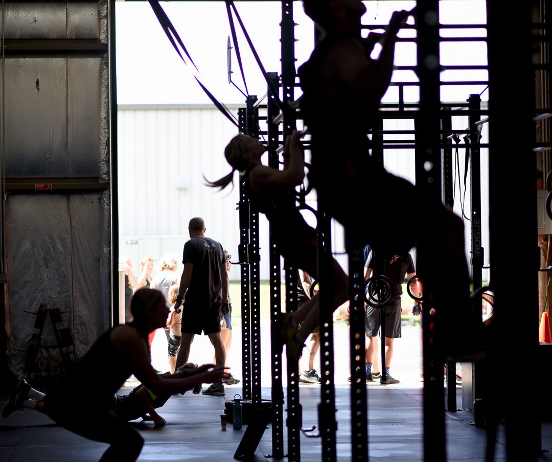 Silhouettes of athletes exercising on gymnastic rings in a CrossFit gym.