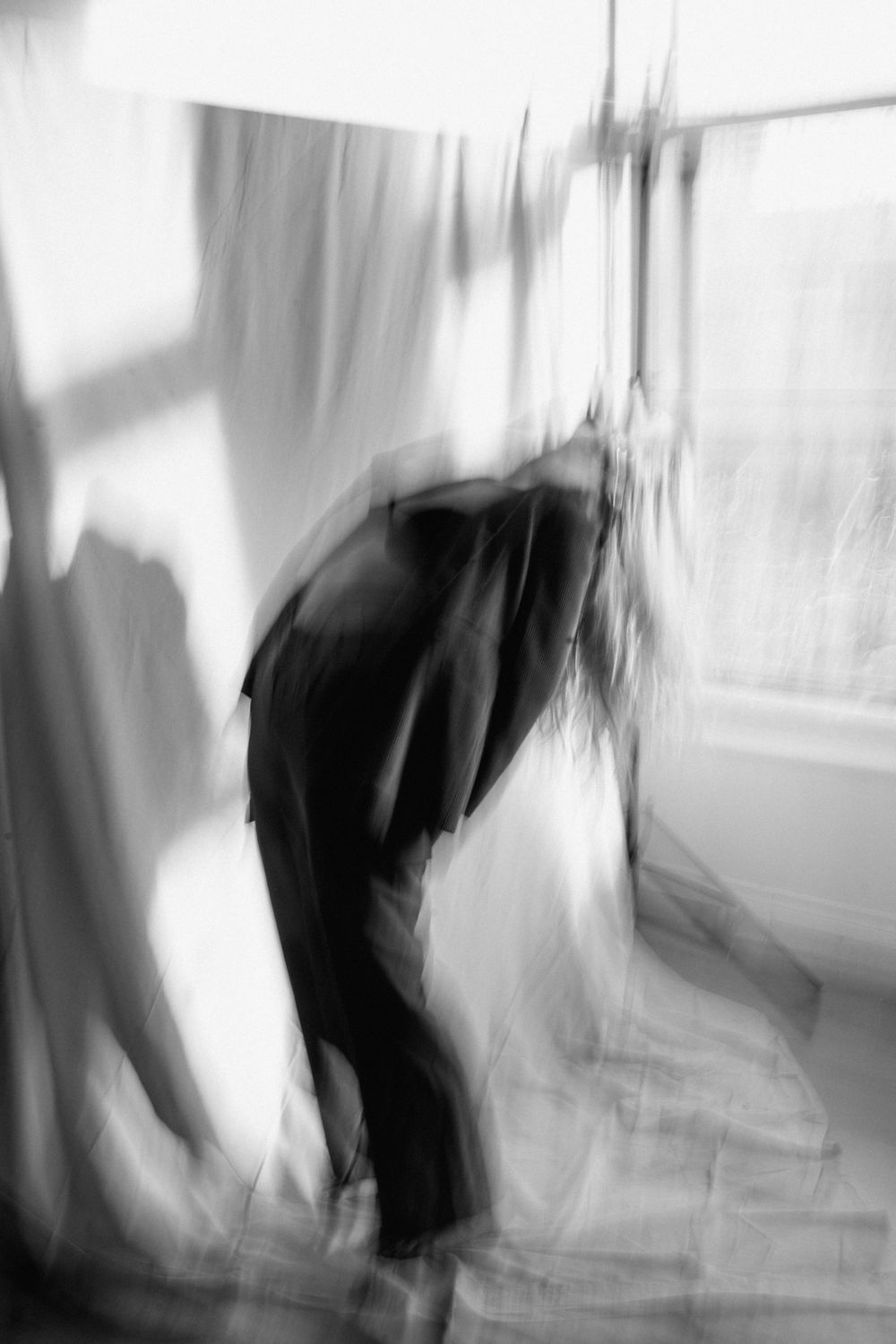 Abstract black and white motion blur photograph showing a bending figure against a bright window.
