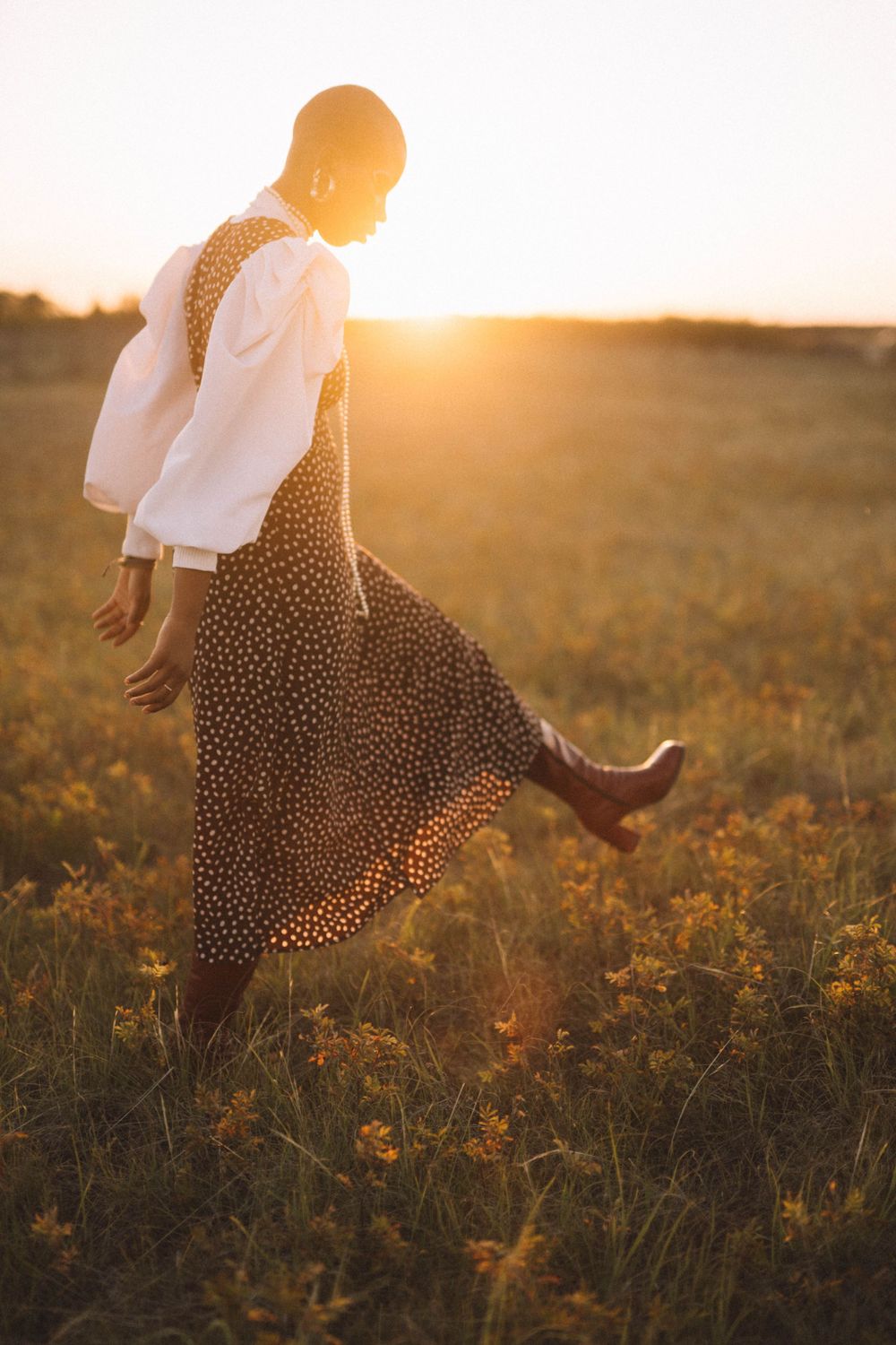 Figure in a flowing polka dot dress dancing in a golden sunset field.