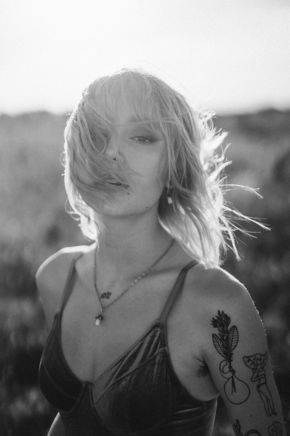 Artistic black and white portrait with backlighting highlighting windswept hair and tattoos.