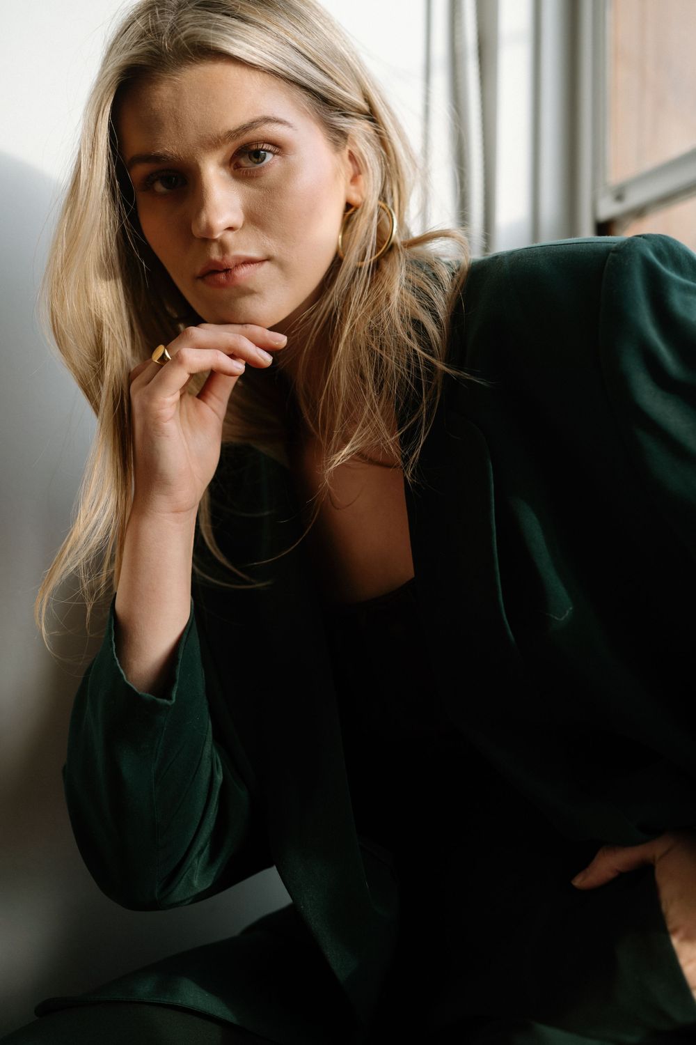 Portrait of someone in an emerald green blazer by a window with soft natural lighting.