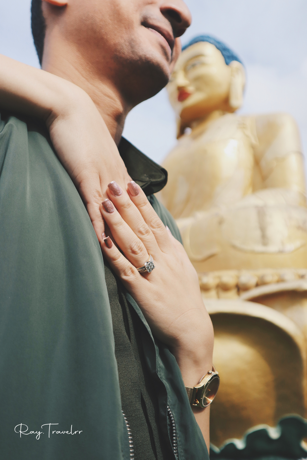 Hand displaying engagement ring with golden Buddha statue in background at temple.