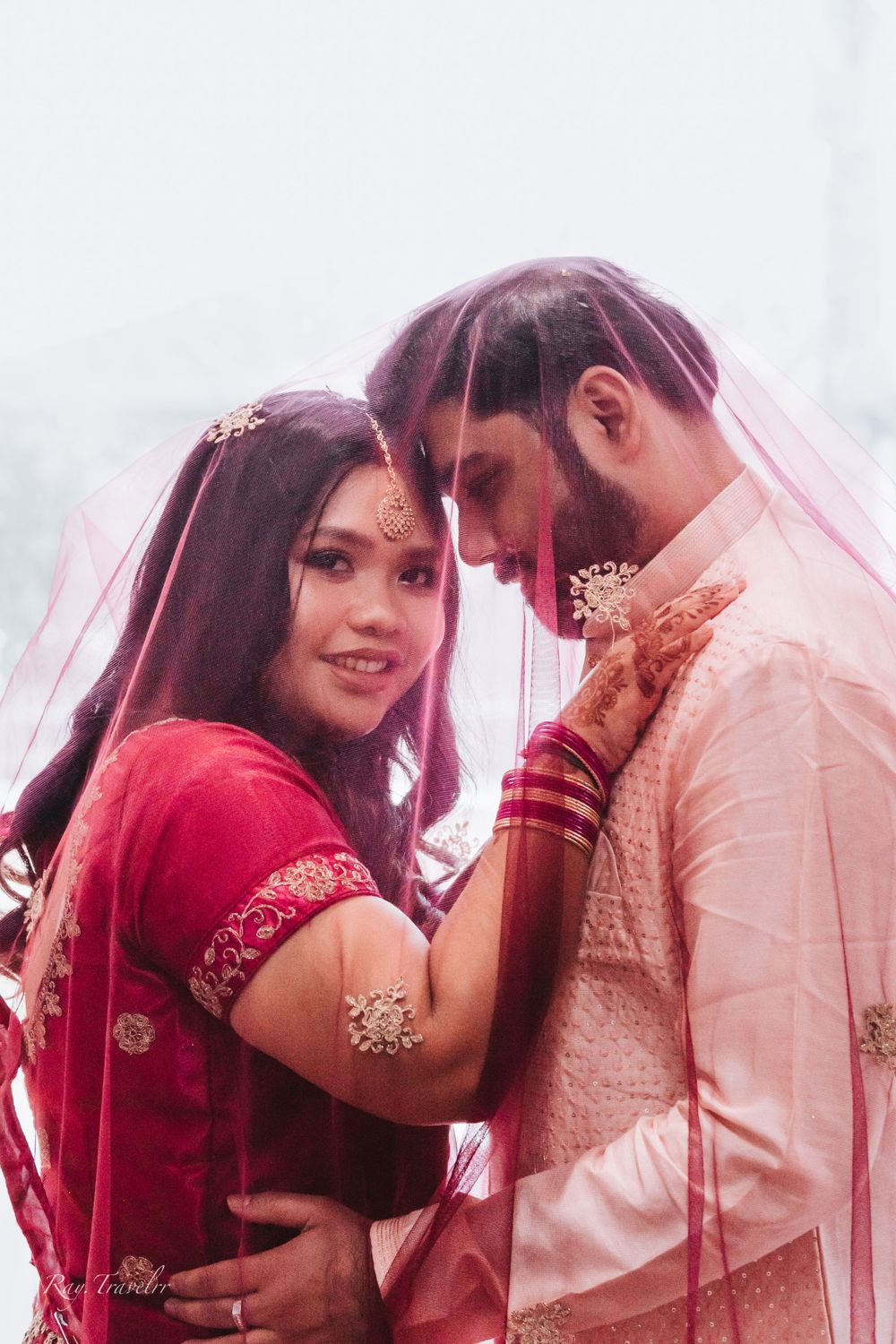 Traditional South Asian wedding couple in red and white attire share an intimate moment.