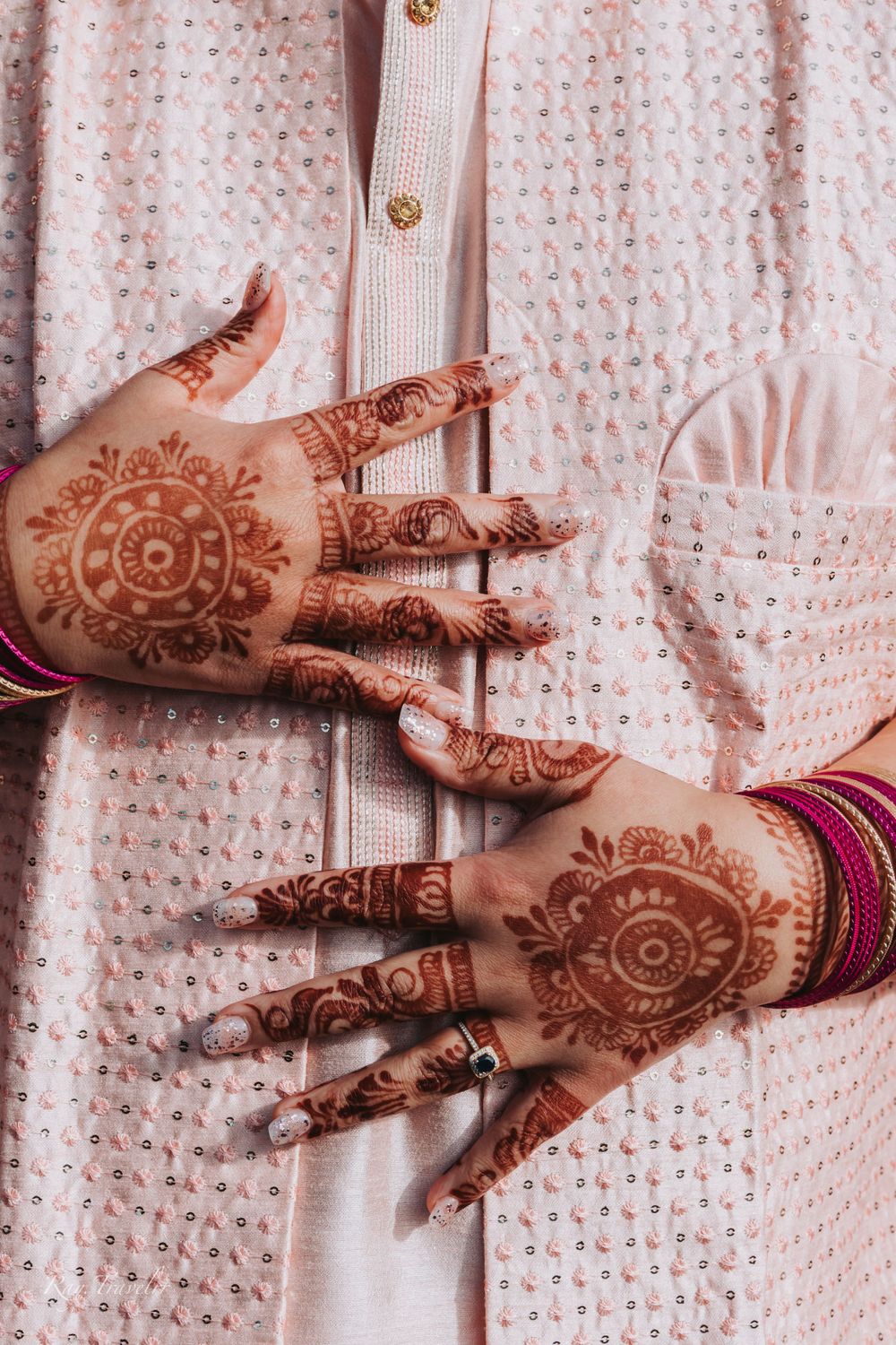 Detailed shot of traditional henna designs on hands against embroidered fabric.