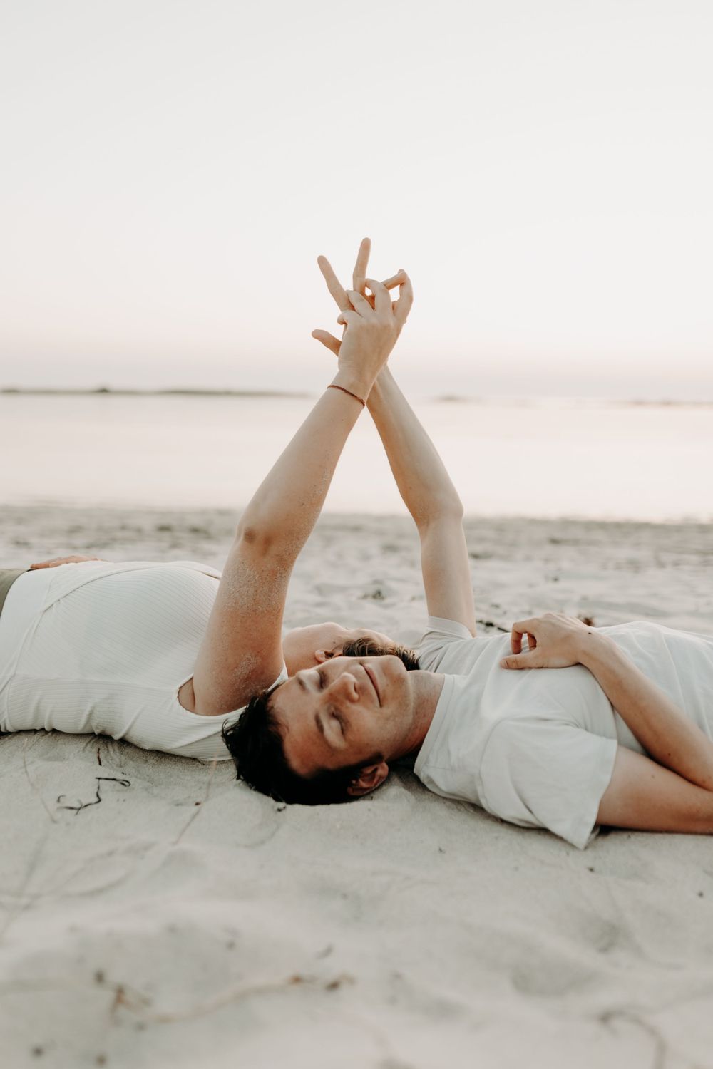 Person lying on sandy beach making peace signs while enjoying a carefree moment.