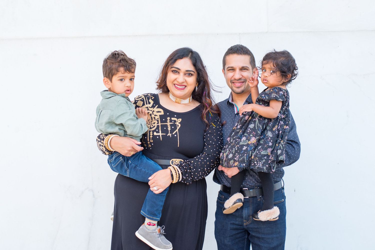 each parent holding a child, family looks on in front of white wall