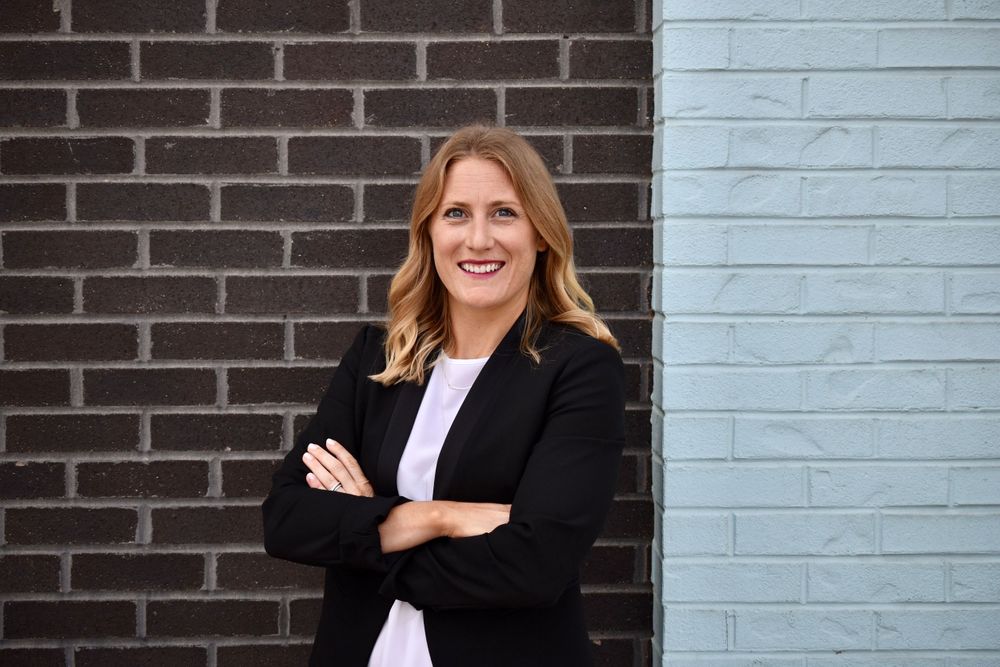 Business professional poses against brick and painted wall background.