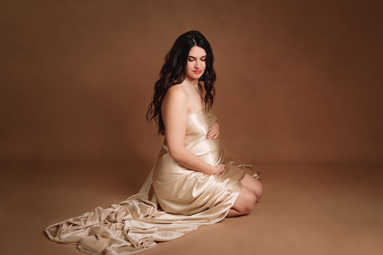kansas city maternity photographer studio maternity photoshoot of woman kneeling draped in gold fabric