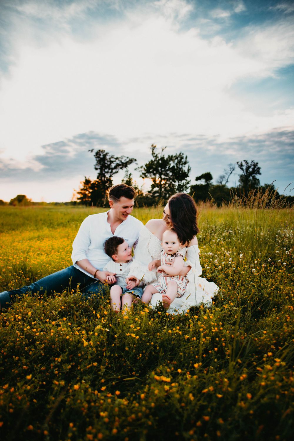 Family laying in yellow wildflower meadow under blue sky.