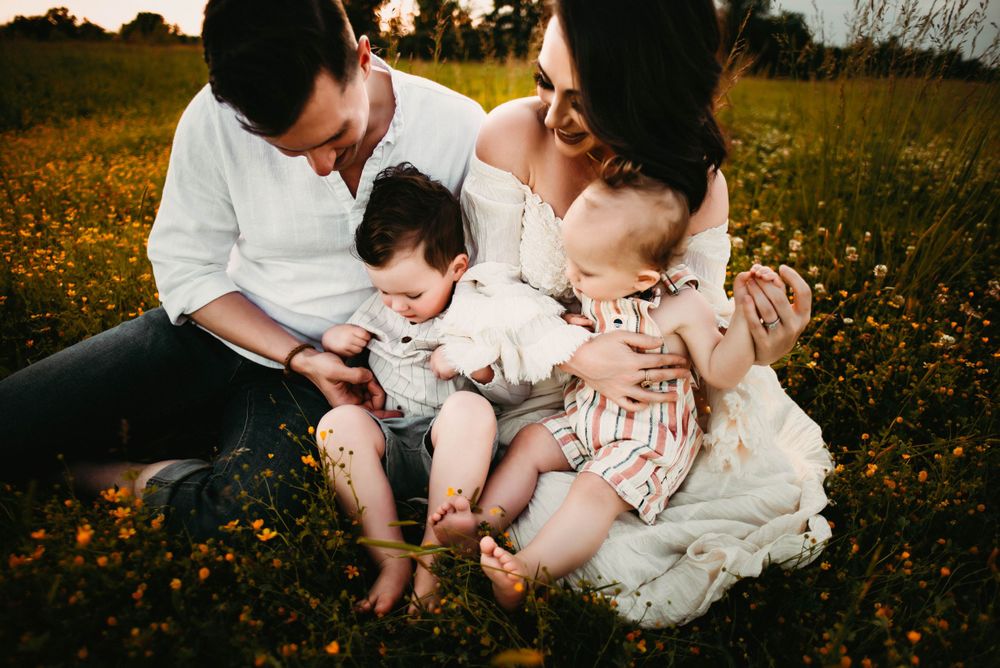 A family shares tender moments together while sitting in a golden wildflower meadow at sunset.