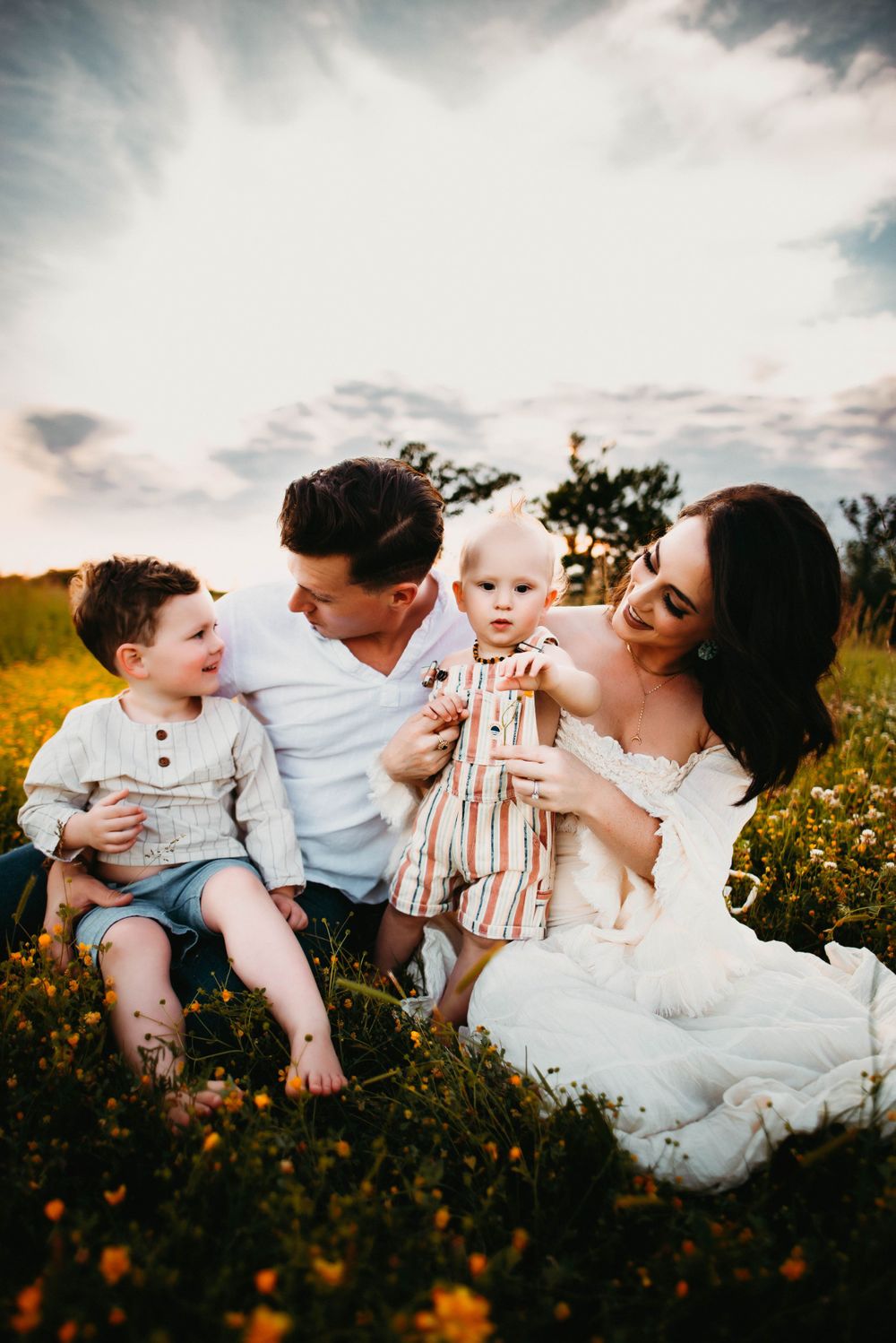 Natural family photography in a rustic field setting with dramatic evening sky.