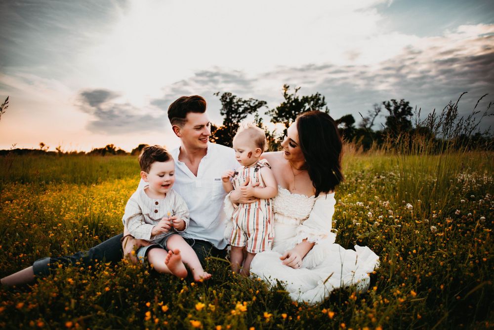 Lifestyle family portrait session in a meadow with dramatic cloudy sunset backdrop.