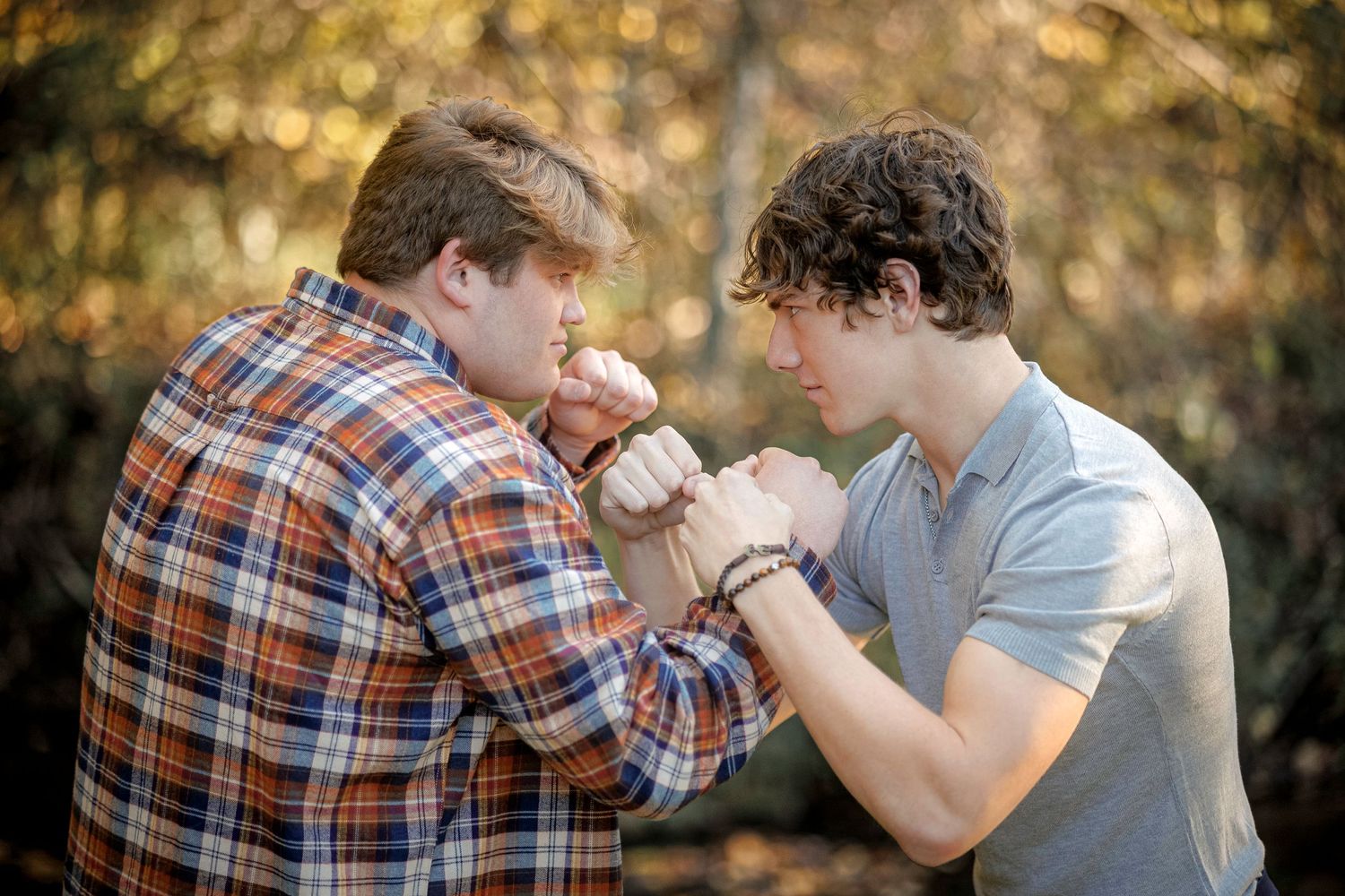 Two people arm wrestling outdoors with autumn foliage in the background.