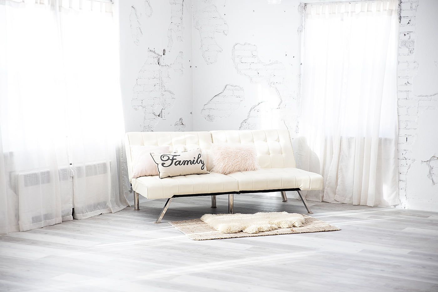 Minimalist white room with a modern beige sofa and sheer curtains filtering natural light.