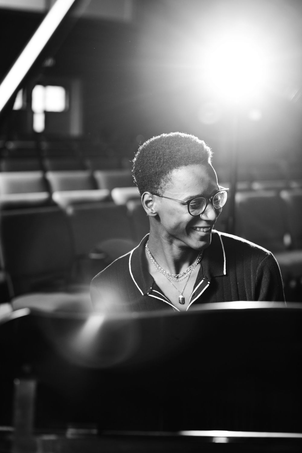 Black and white portrait of musician at piano with dramatic side lighting and warm expression.