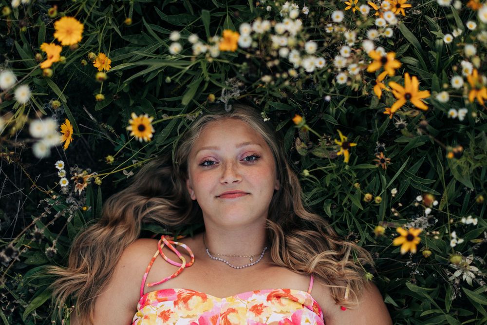 Artistic portrait surrounded by yellow and white wildflowers in garden setting.