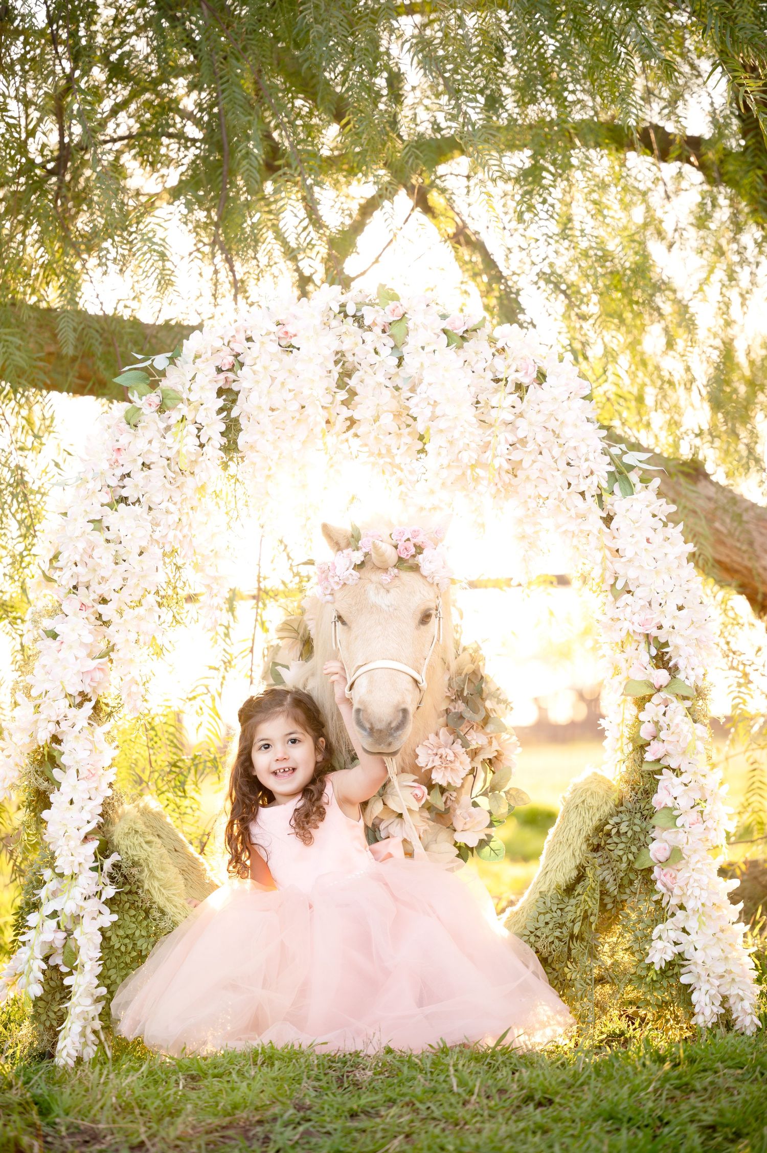 Magical garden portrait with white pony under floral arch and flowing pink dress.