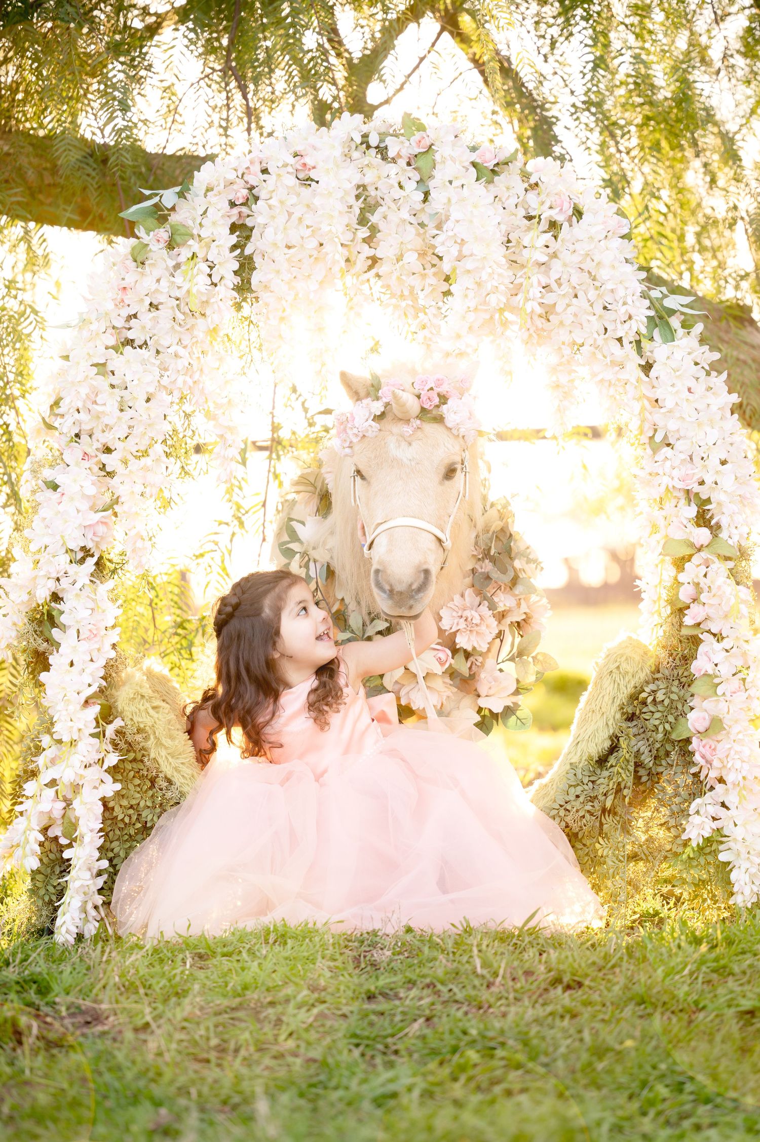 Dreamy garden scene with decorated pony and pink tulle dress under white floral archway.