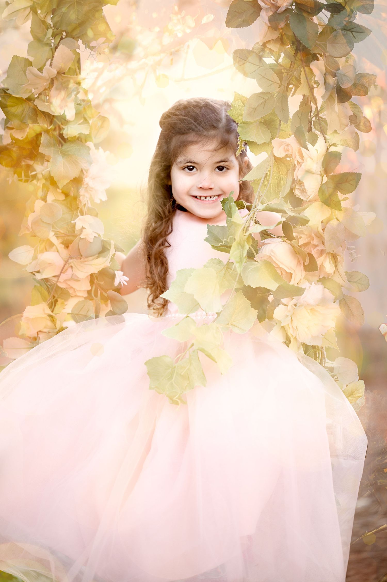 Ethereal portrait in pink tulle dress amid soft golden foliage and flowers.