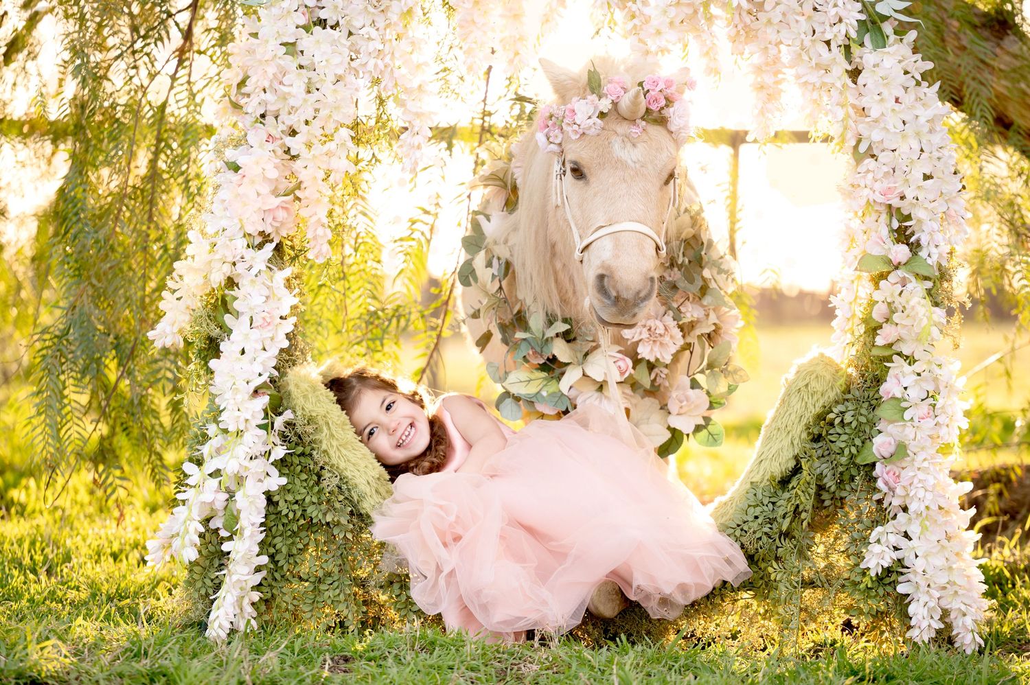 Dreamy portrait with white pony and pink dress amid hanging wisteria flowers at sunset.