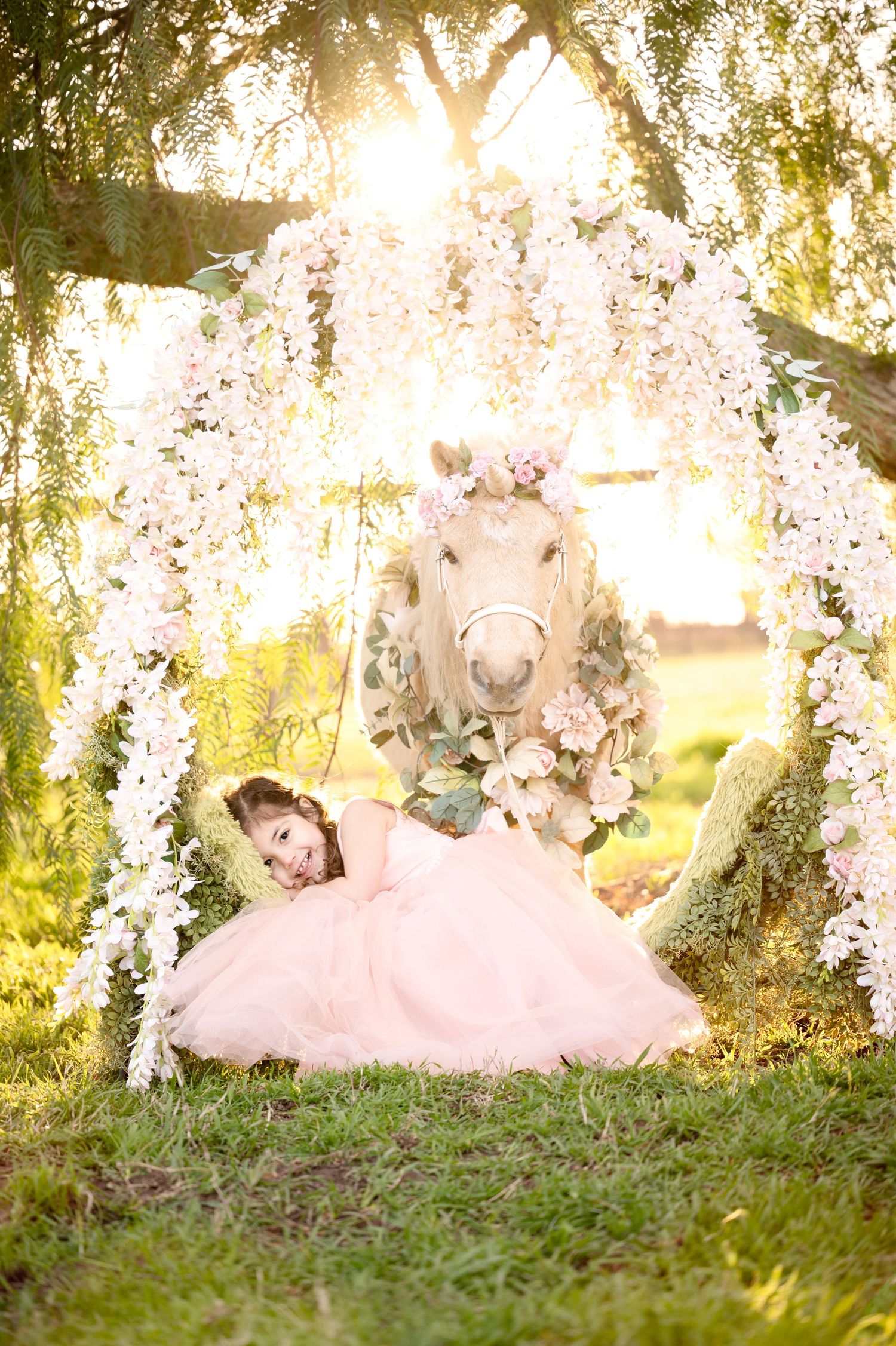 Enchanting sunset scene with floral arch, pink tulle dress, and decorated white pony in garden.